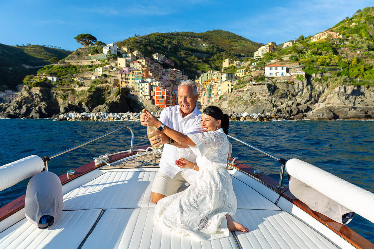 Couple on a boat celebrating with Prosecco in front of Riomaggiore, Cinque Terre